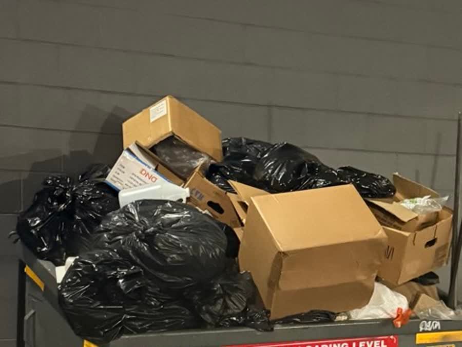 Building dumpster overflowing with bagged trash and boxes